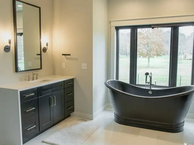 Bathroom with a black slipper claw foot tub under a large window and a dark custom vanity with white top