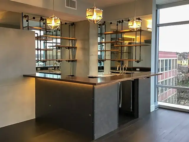 Loft-style kitchen design with a dark island, warm under-counter lighting, open pipe shelving and tall windows