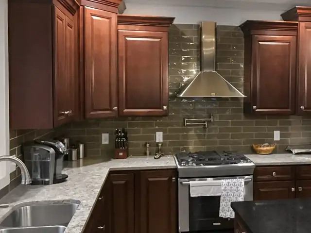 Cherry raised-panel kitchen cabinets with glass subway tile backsplash, granite counters and a stainless hood
