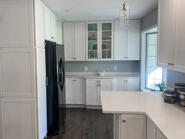 White Shaker kitchen with glass-front upper cabinets, quartz peninsula and dark wood floor