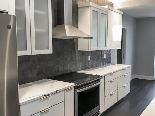 White and gray kitchen with dark handmade-look tile backsplash, stainless hood and quartz counters