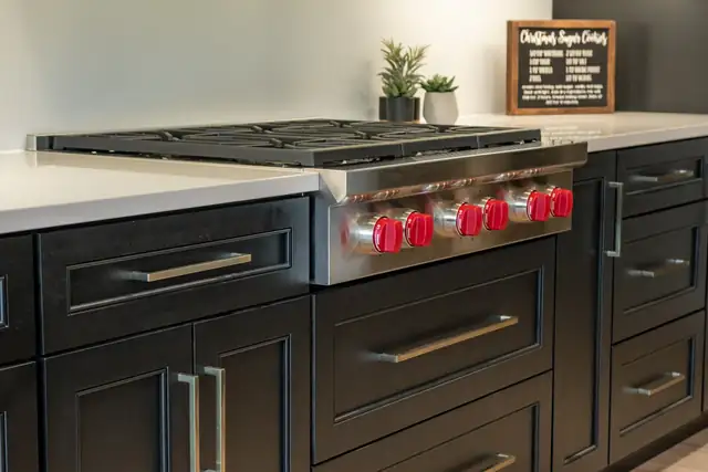 Professional gas rangetop with red knobs set into black shaker cabinets with a white counter