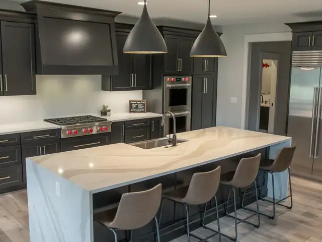 Kitchen with charcoal cabinets, a waterfall quartz island with seating, professional range and black pendant lights