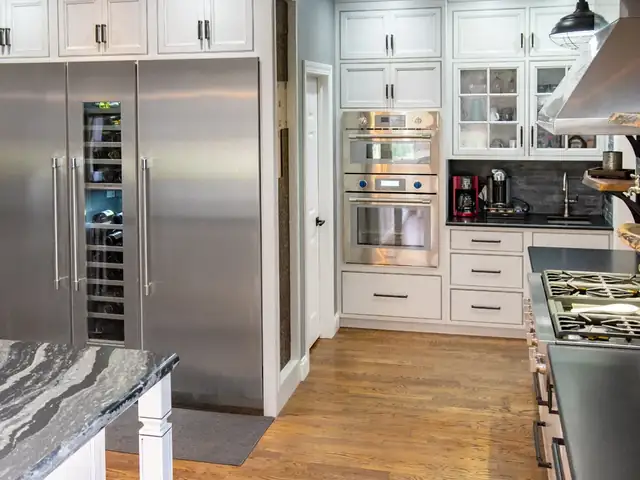 Built-in stainless refrigerator and wine column with white cabinets and double wall ovens